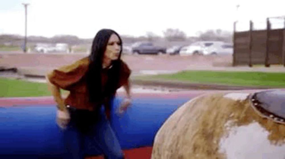 a woman is standing next to a bull on a rodeo simulator .