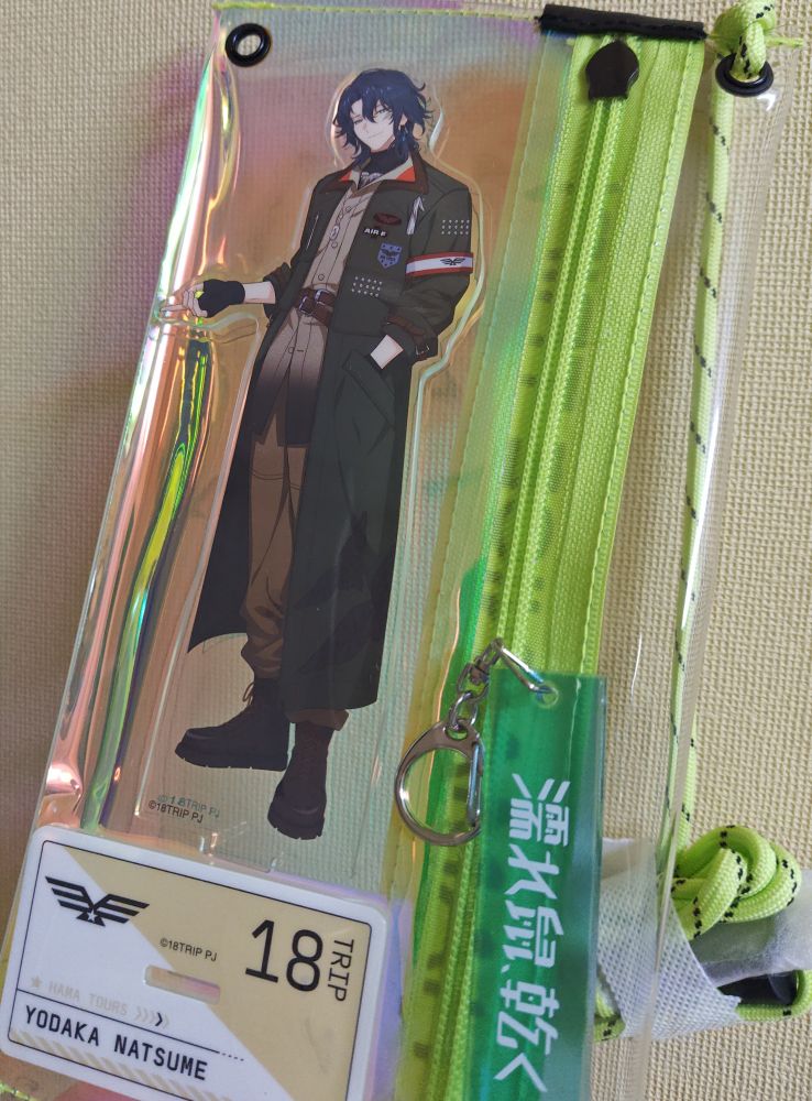 アプリゲーム「エイティーントリップ」に登場する棗夜鷹さんのアクリルスタンドと、寮の部屋名「濡れ鼠、乾く」のキーホルダーを透明なサコッシュに入れた写真。