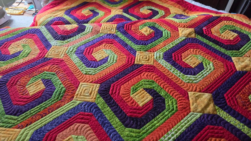 Quilt with orange, green, purple, and chili red spirals, with yellow squares in between the spiral blocks.