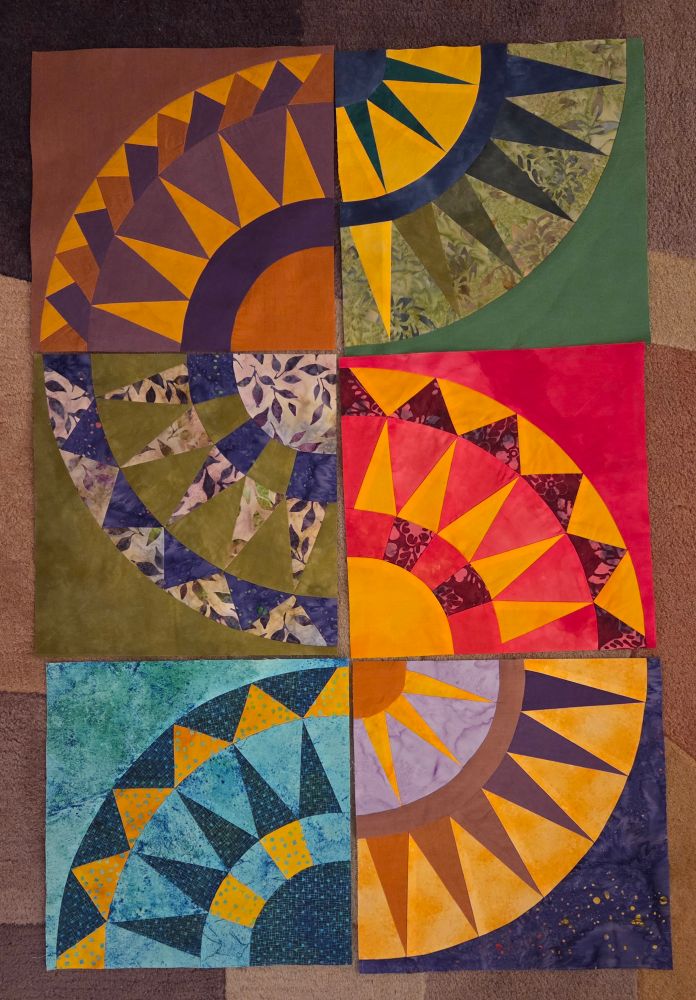 Six New York Beauty quilt blocks of various colors and patterns laying on the rug.