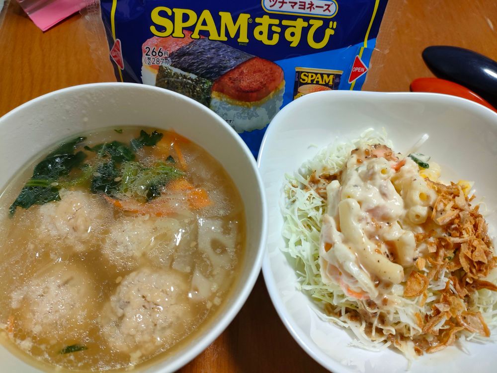 左側は、鶏団子が入った野菜たっぷりのスープ。右側は、マカロニサラダとフライドオニオンがキャベツの千切りに乗っている。背景には、ツナマヨネーズ味のSPAMおむすびが写っている