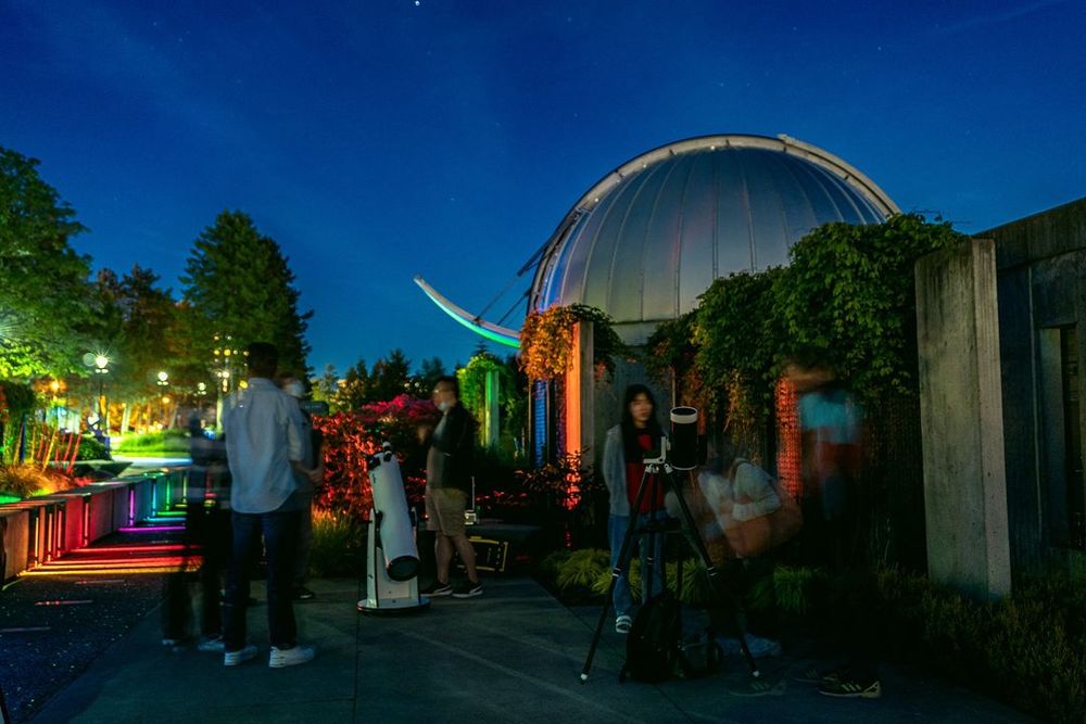 The Trottier Observatory with the dome hatch open at night. There are people and telescopes standing in the courtyard in front of it and everything is lit up with rainbow colours to represent the spectrum of the sun. Photo: Martin Curic