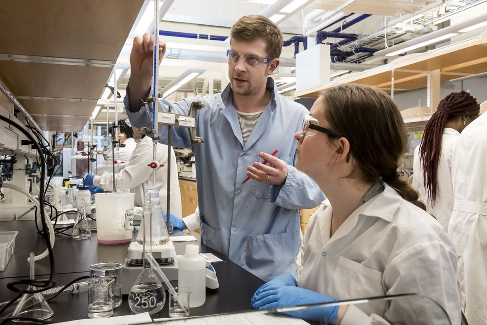 An instructor in a chemistry lab demonstrates how to use lab equipment to a student