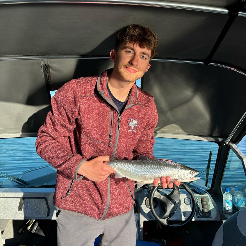 Matthew Lemp smiling, standing on a boat, holding a trout.
