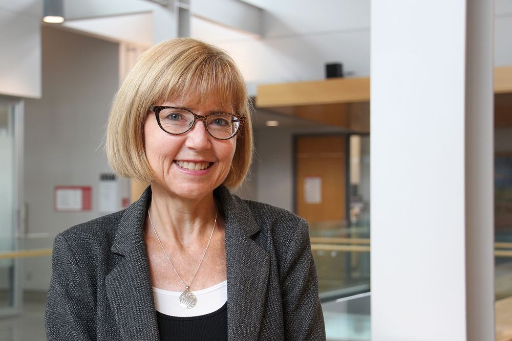 Portrait of Fiona Brinkman, a smiling, middle-aged woman with jaw-length blonde hair and glasses wearing a grey blazer.