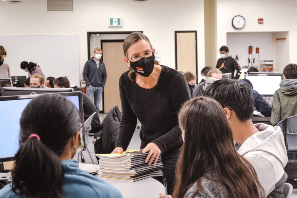 SFU Physics professor Nancy Forde gathers a stack of booklets from students in a classroom