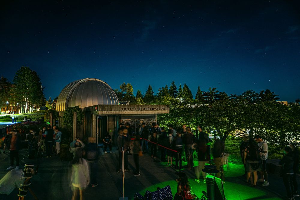 Starry Nights at the SFU Trottier Observatory. There are approximately one hundred people standing in the courtyard around the observatory dome, dimly lit by green lights.