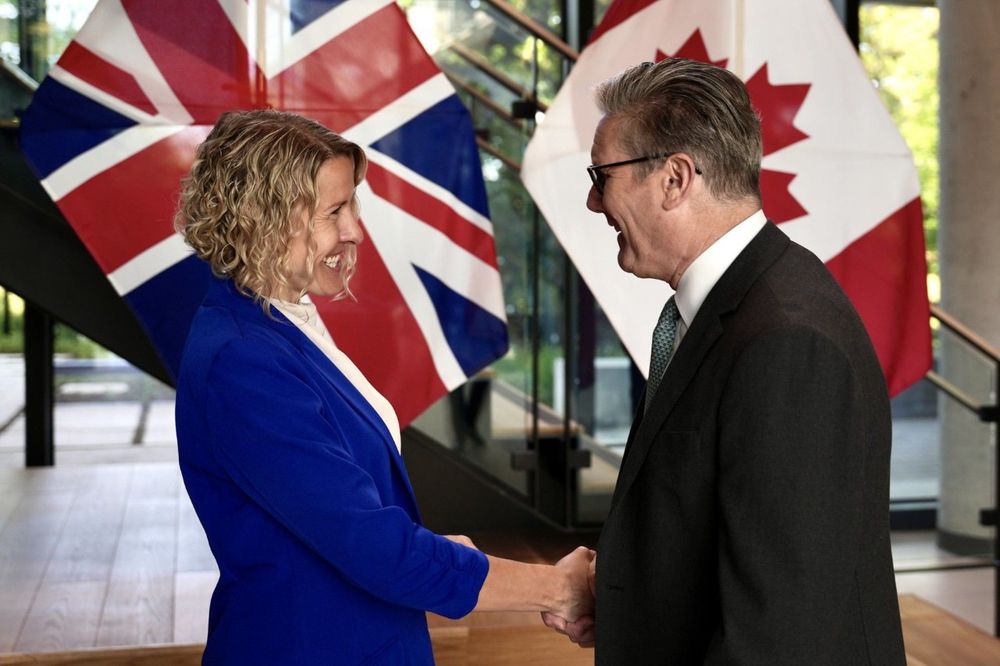 SFU associate professor Stephanie Simmons is smiling widely as she shakes hands with with U.K. Prime Minister Keir Starmer at the British High Commission, in Ottawa. The Canadian and UK flags are draped in the background.