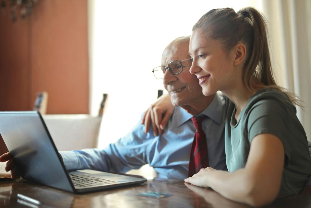 yngre person hjælper ældre med arbejde på computer. 