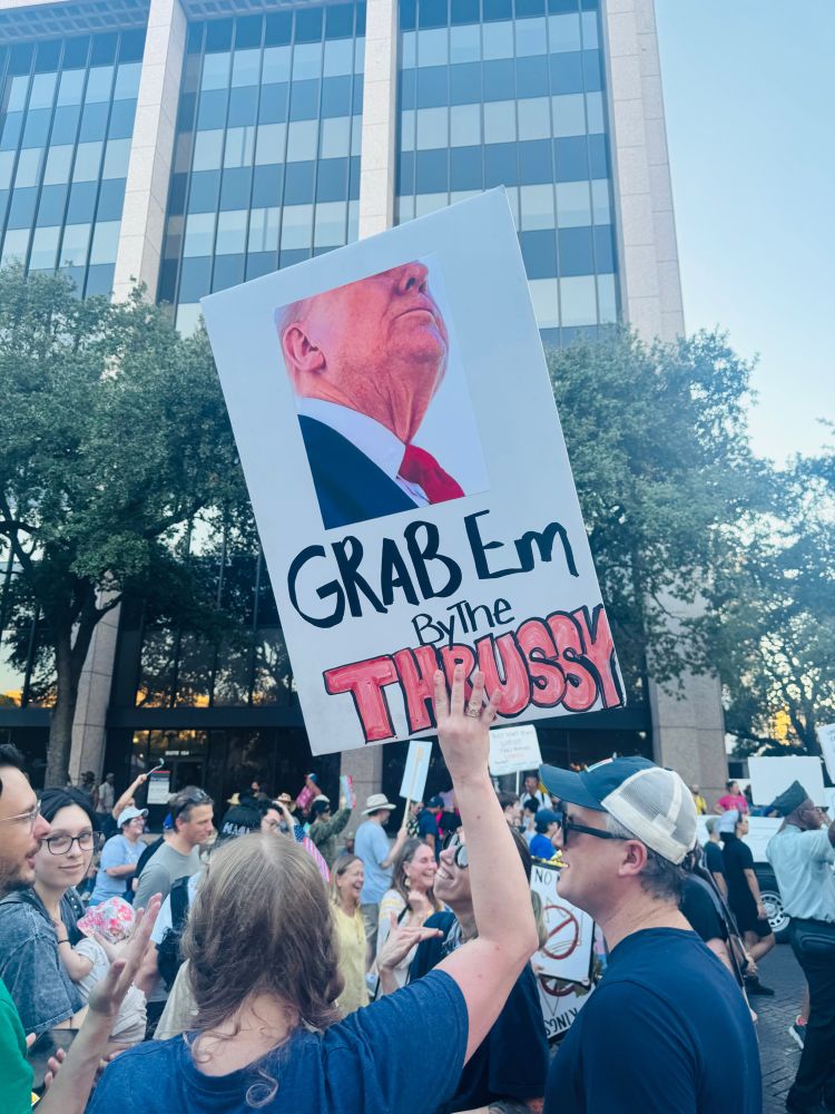 A protester holds a sign featuring a photo of Donald Trump with the phrase “Grab ’em by the thrussy” written below.