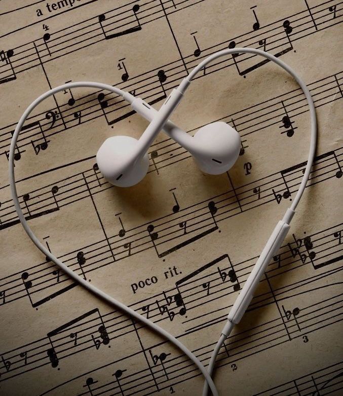 White earphones are arranged in the shape of a heart on top of a sheet of music.