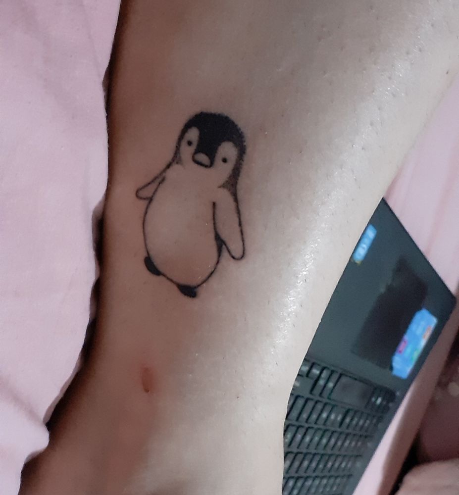 Foto do meu tornozelo, em que tem uma tatuagem de pinguim, bem simples com traço preto