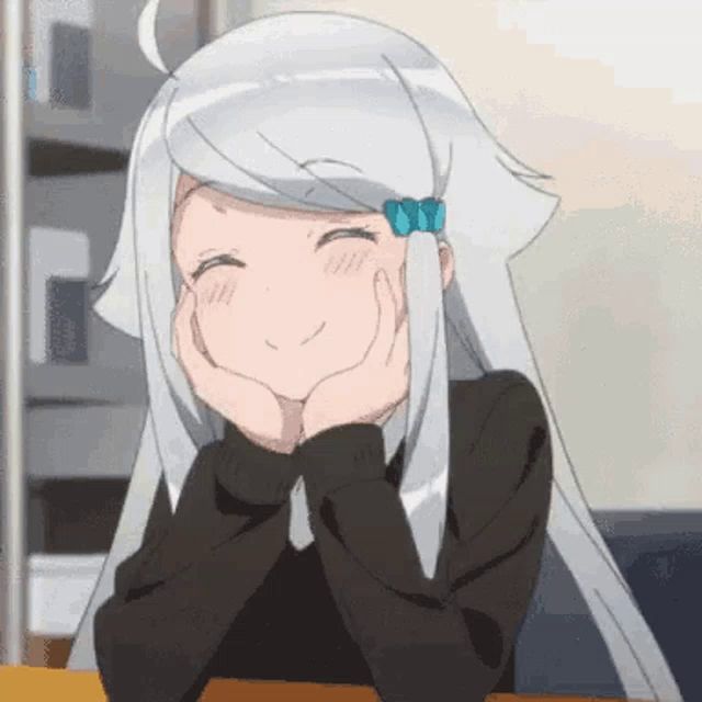 a girl with white hair is sitting at a table with her hands on her face and smiling .