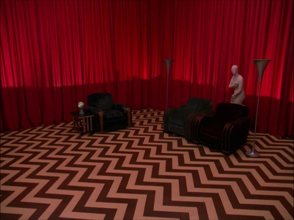 Twin Peaks Black Lodge red room. Black and white zigzag patterned floor, three black chairs, statues and red curtains 