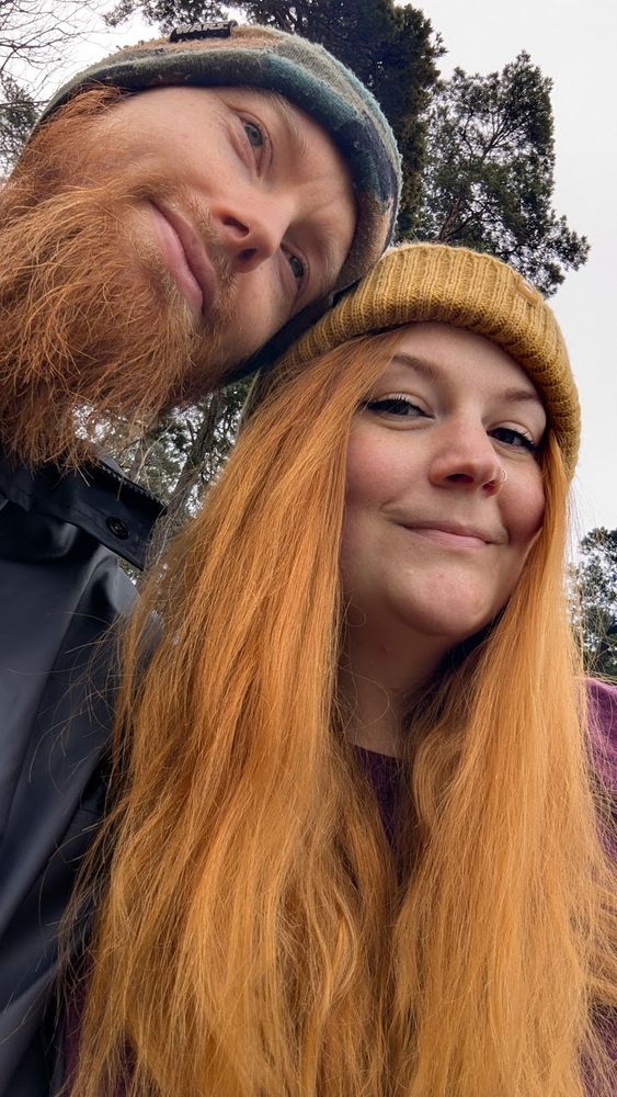 Two people with copper toned hair sit together outside.