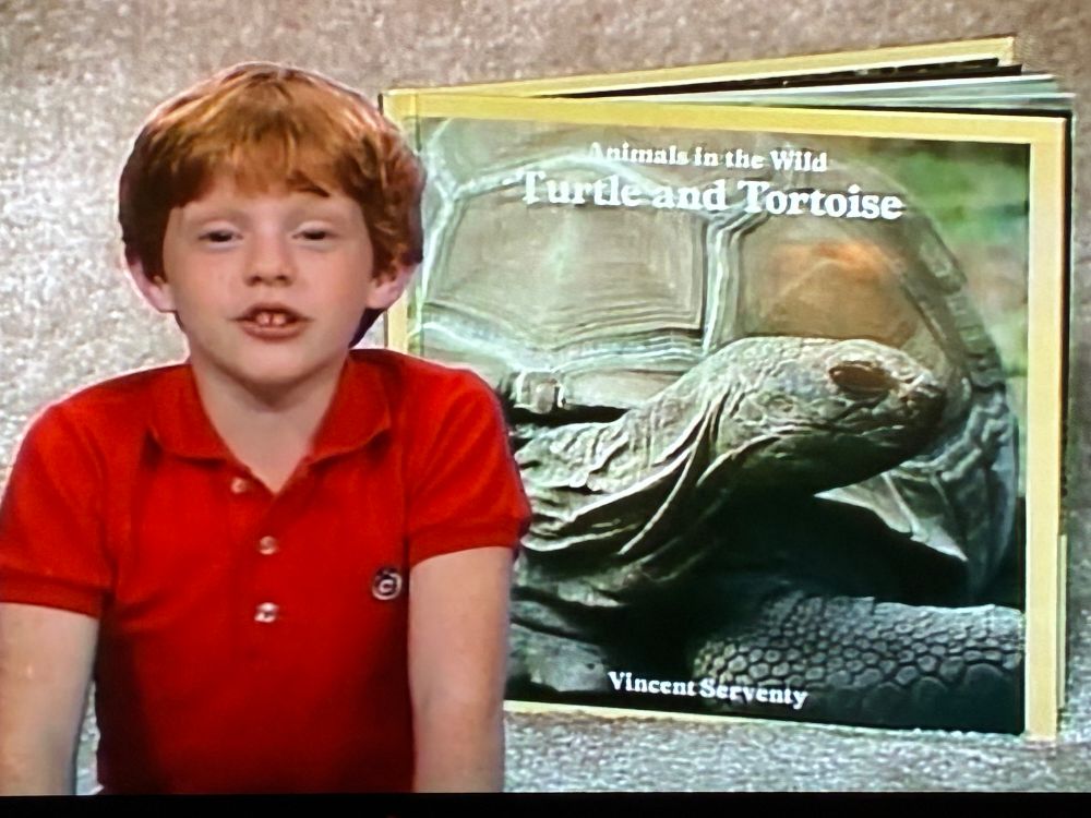 Handsome young man in a red polo shirt talking about an Animals in the Wild book entitled “Turtle and Tortoise” by Vincent Serventy