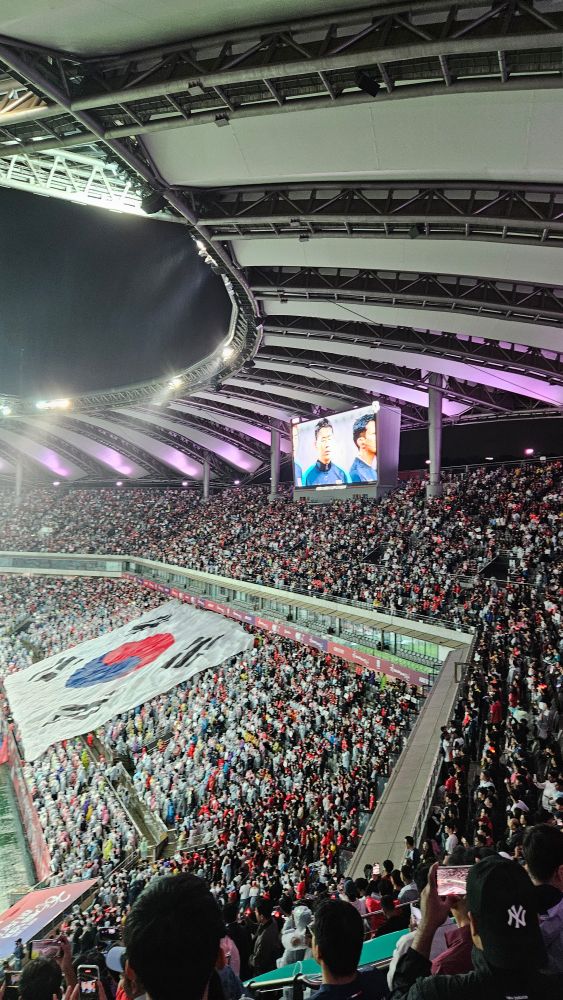 Sonny on the big screen, huge crowd in the rain, the Korean flag being unfurled for the national anthem before the game.
