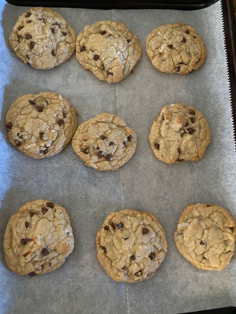 9 chocolate chip and shredded coconut cookies are shown sitting in a baking sheet on top of parchment paper 