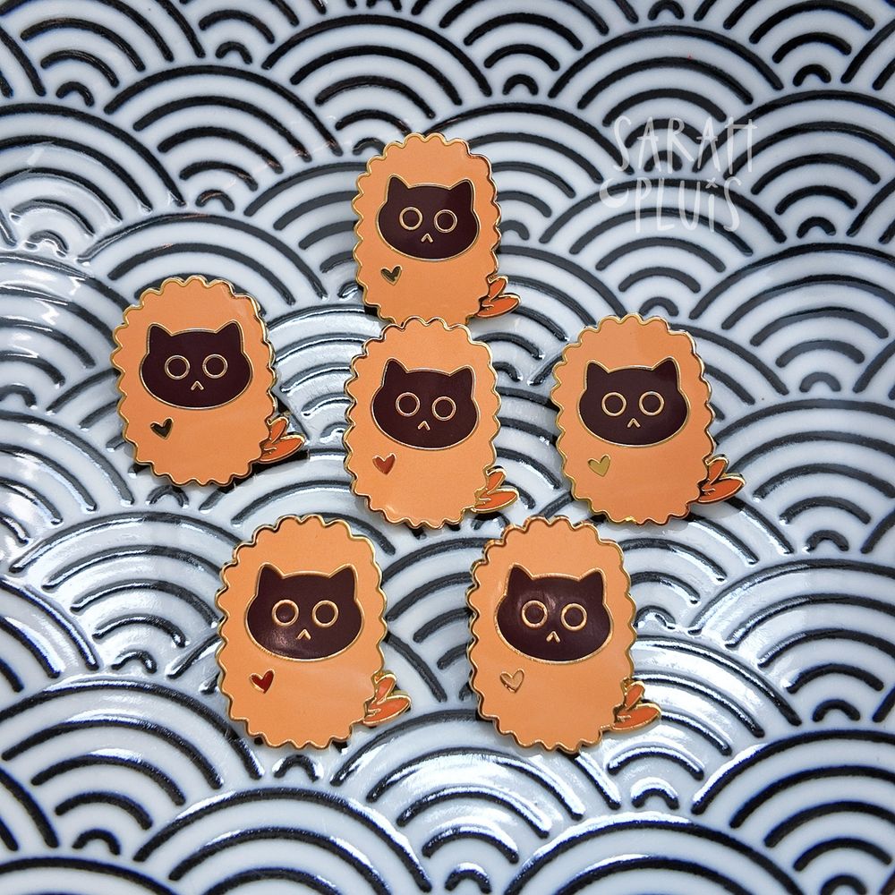 5 Pins mit Katzenmotiv liegen in einem Teller mit Wellenmuster.