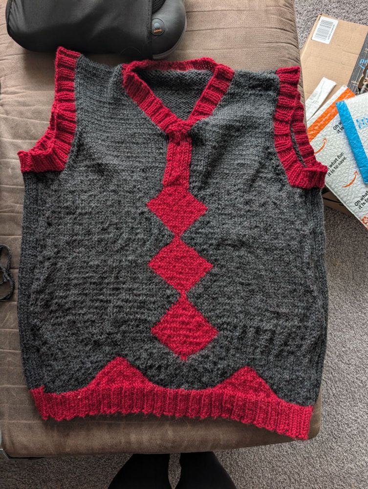 An physical knitted sweater vest in dark grey and red in the style of Hassel from Pokemon Scarlet and Violet's sweater vest 