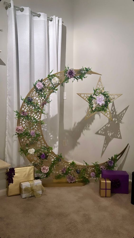 An about 4 feet tall, golden metallic crescent and star , embellished with lilac, pink purple flowers and green leaf decor, with gifts put under it. For festival of Eid on completion of the Holy month of Ramadan.