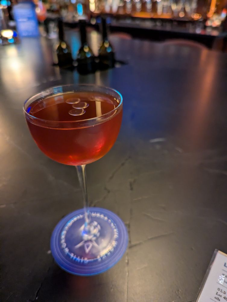 A red cocktail in a Nick & Nora glass on a bar.