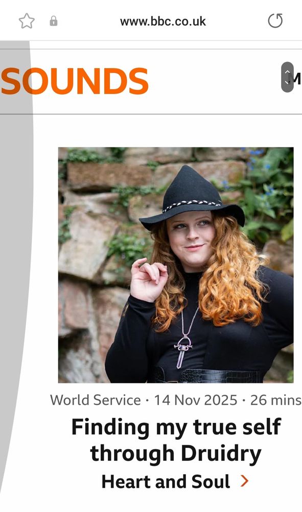 A closer screenshot of the BBC website, showing a lovely photograph of the glorious Mhara Starling, who is wearing a black low, pointy hat, black top and very wavy hair. She is smiling and looks beautiful. The title of the BBC Sounds piece is "Meet Mhara who found her true self through Druidry".