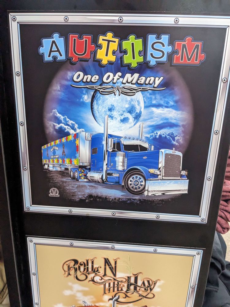 Ad for shirt that depicts a semi truck backgrounded by a glowing moon.  Above it are the words “AUTISM: One of Many”
