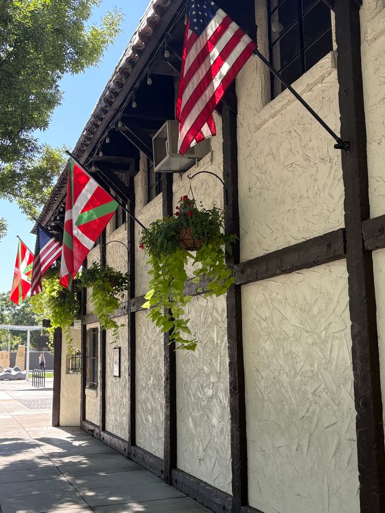 Basque and American flags alternate along a building. The Basque flag is red with white and green stripes crossing it, the white from top to bottom and side to side, and the green diagonally.