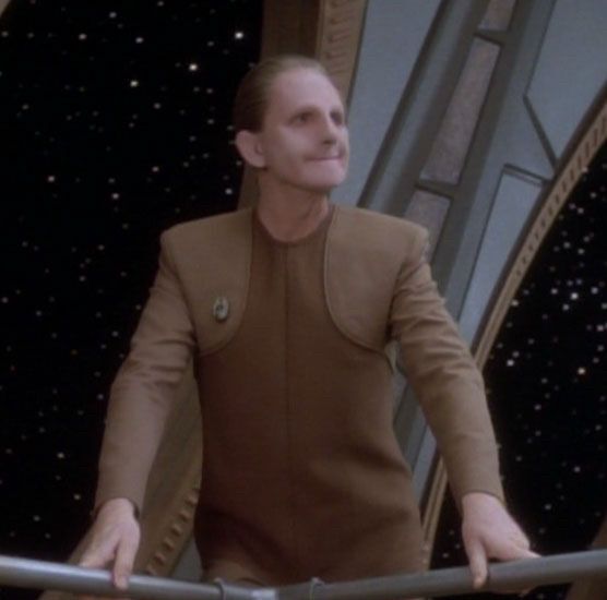 A picture of Odo from Star Trek Deep Space Nine leaning on a guardrail on the Promenade while smiling quite adorably 