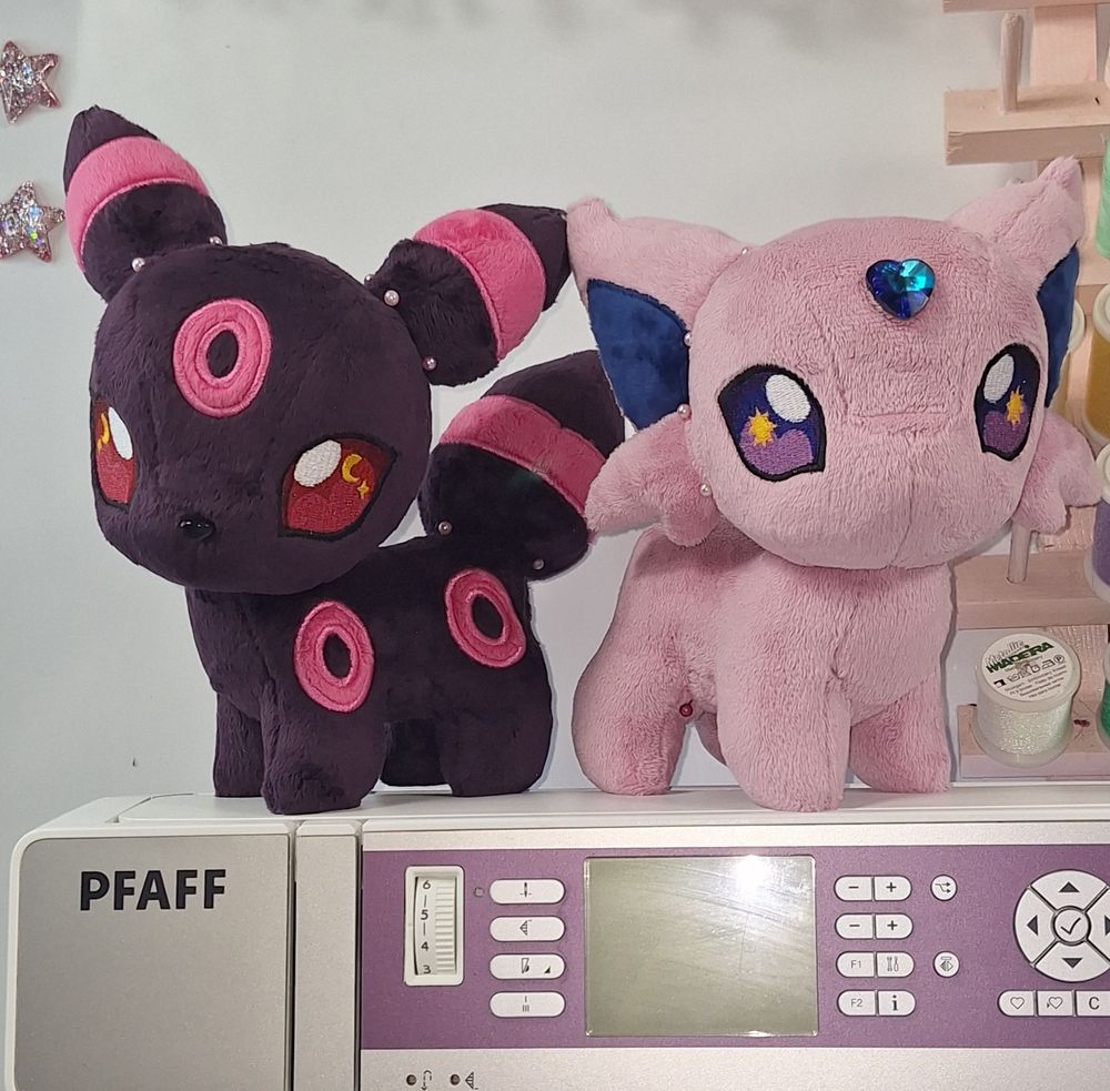 #WIP shot of two chibi plush, a dark berry purple Umbreon with neon pink rings and a dusty rose Espeon with a blue heart shaped gem on its forehead. Loosely based on their BETA design descriptions. The Espeon has no nose yet, or any face sculpting. #plushart 