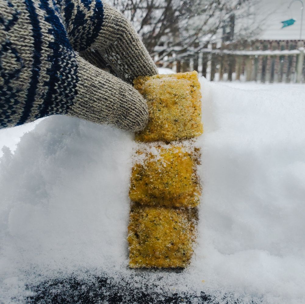 A hand using three toasted ravioli to measure snowfall