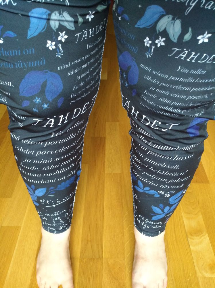 Middle aged legs wearing leggings that are mostly black, but with poetry in Finnish & Swedish printed on them, in different fonts. 