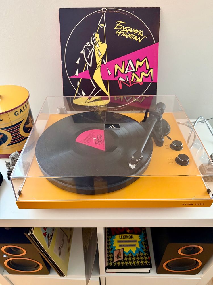 Bakom en gul skivspelare där en skiva snurrar står omslaget till Ensamma Hjärtans album ”Nam Nam”. 