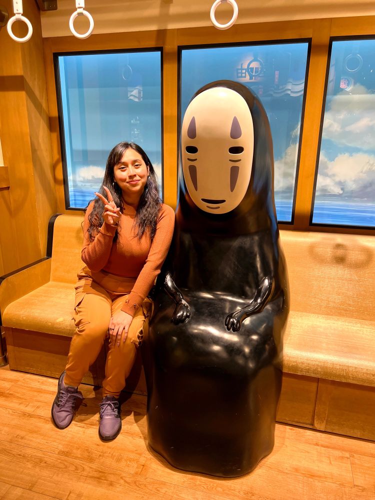 Picture of me doing the peace sign and sitting next to a statue of the character No Face from the movie Spirited Away