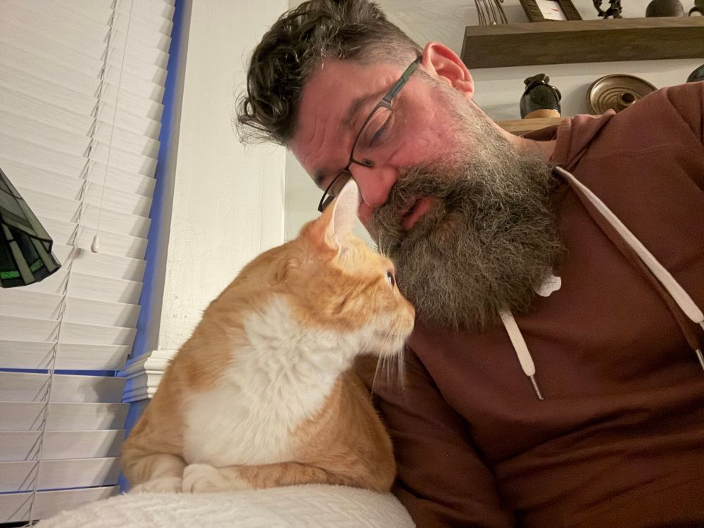 A bearded man, leaning down to be face-to-face with an adorable orange and while kitty [Jack]