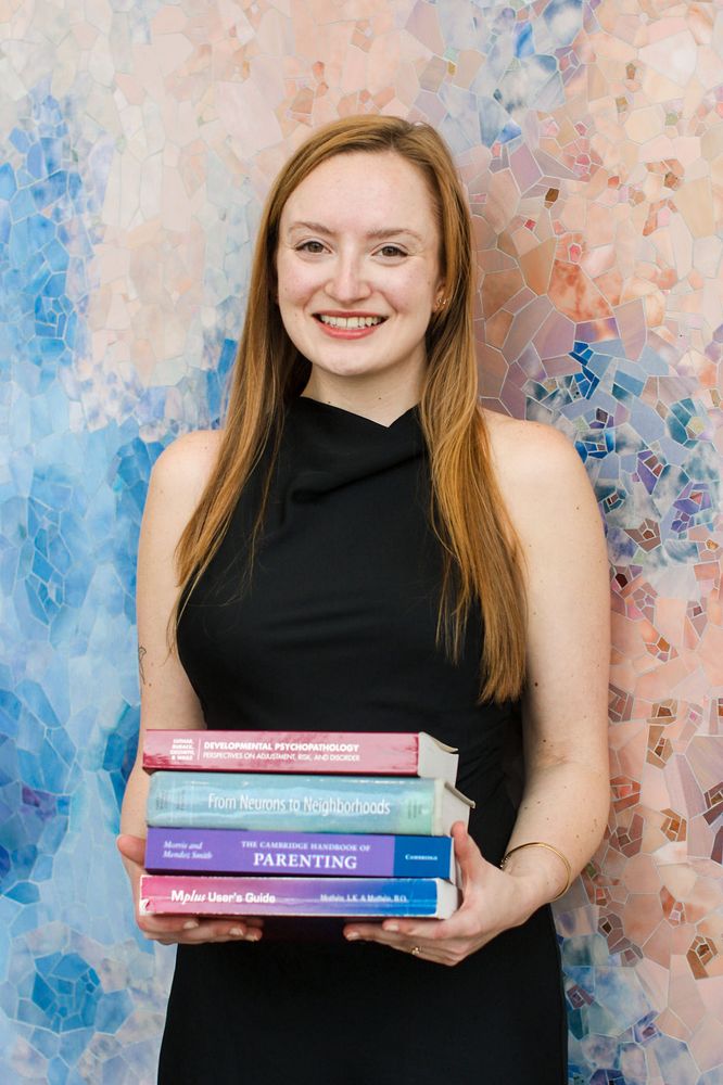 Lilly smiling and holding books about developmental psychopathology