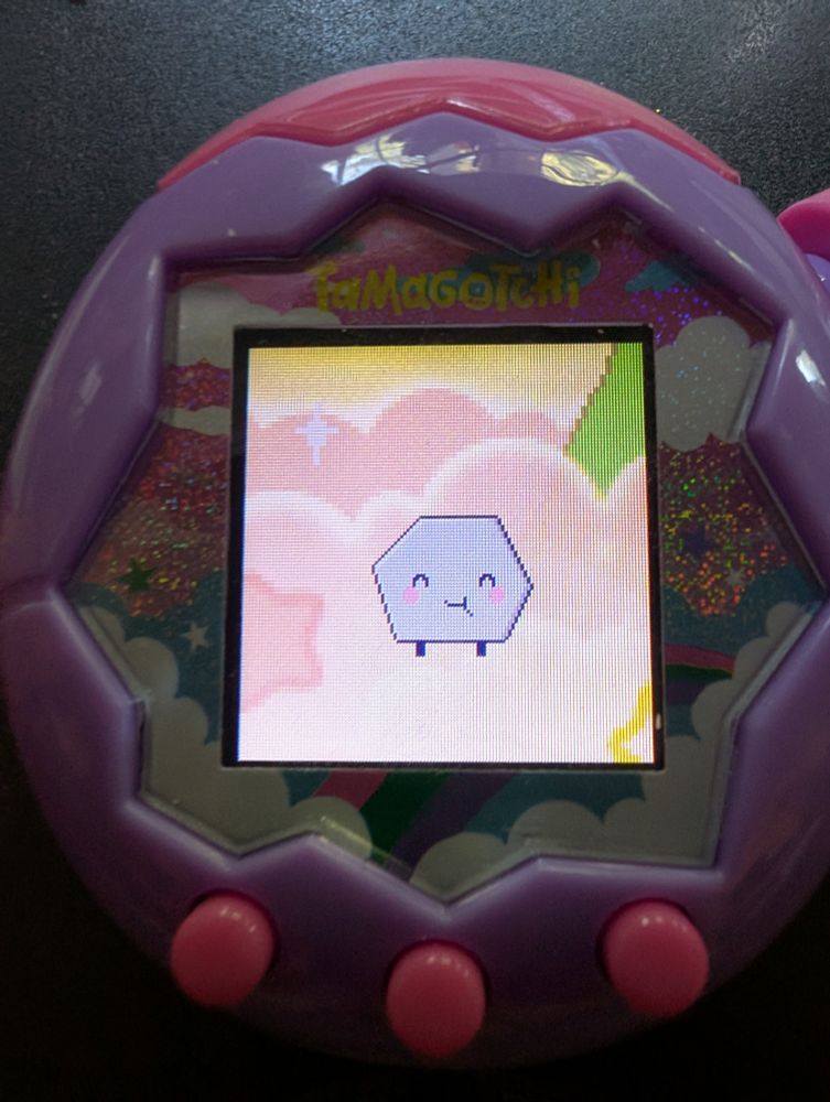 A photo of a Tamagotchi Paradise device, featuring a rock-based tamagotchi in the shape of a hexagon. The Tamagotchi is happy