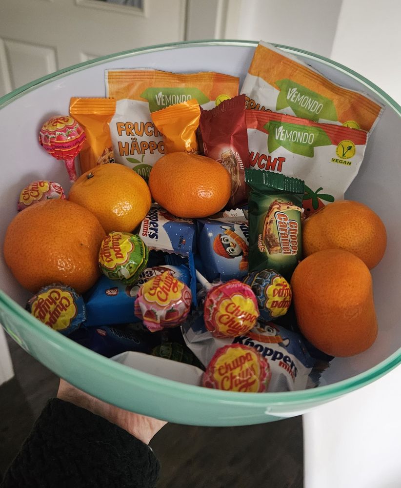 Eine Schale mit einer Auswahl aus Schokoriegeln, Lollies, Fruchtüten und Mandarinen.