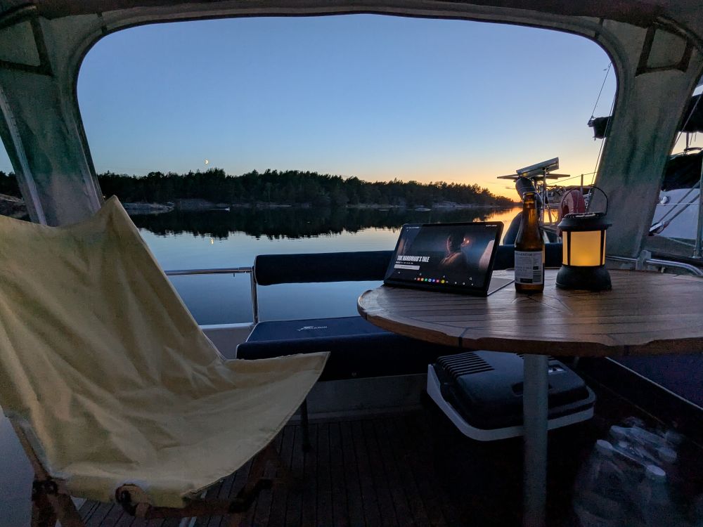 Evening view from a boat. Calm sea, clear sky, a bottle of beer, and a tablet showing A Handmaid's Tale.