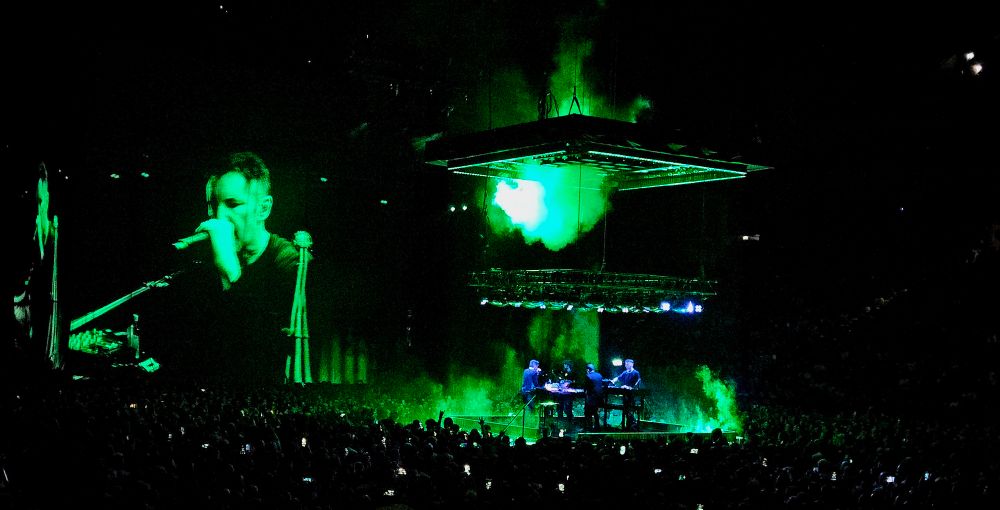 Nine Inch Nails gig set up with green-lit image of Trent on a screen to the left and a raised platform to the right. 
