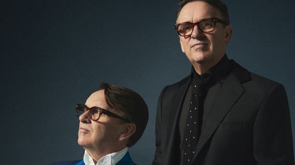 A man sitting and a man standing next to him. It's the same man.