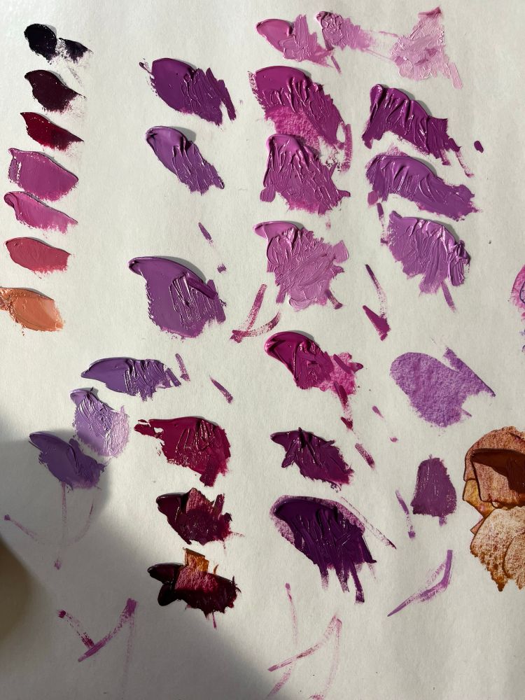 Photo of an artist palette with small piles of mixed paint in varying shades of pinks, purples, and deep red.