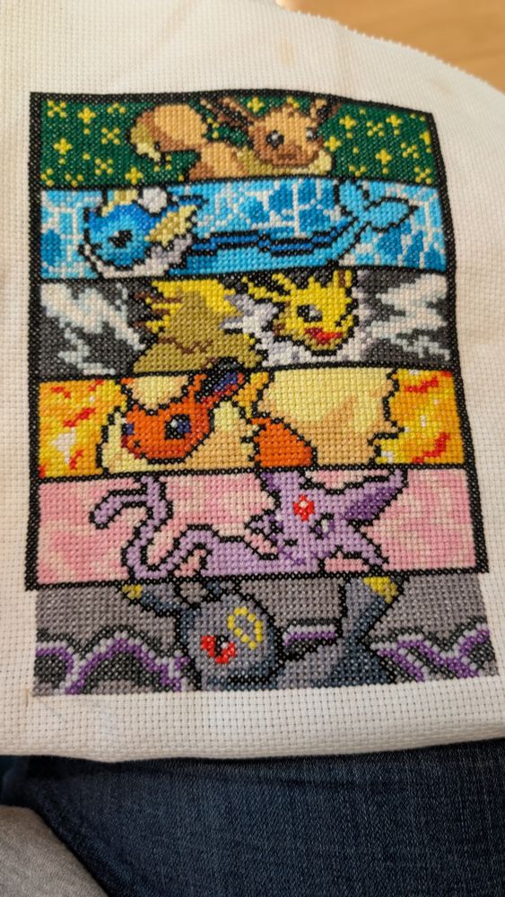 A cross stitch work of Eevee and Eeveelutions. The work has Eevee, Vaporeon, Jolteon, Flareon, Espeon, and Umbreon finished so far. Each pokemon is pixelated with backgrounds representing their type.