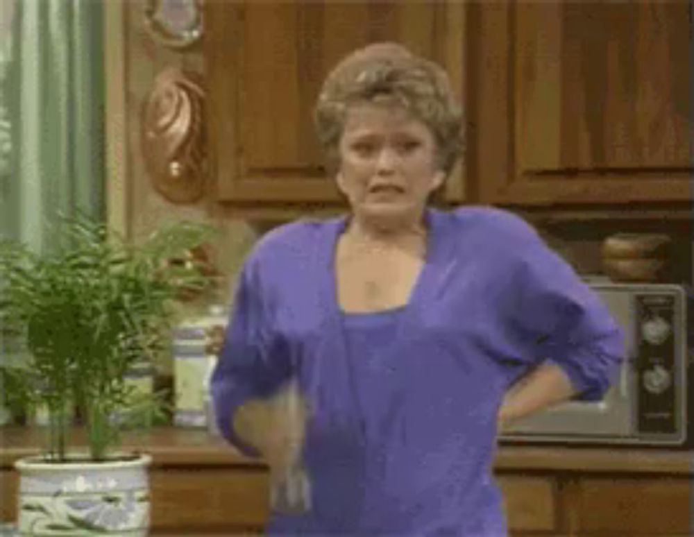 a woman in a purple shirt is dancing in a kitchen