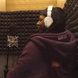 a man wearing headphones stands in front of a microphone and gives a thumbs up