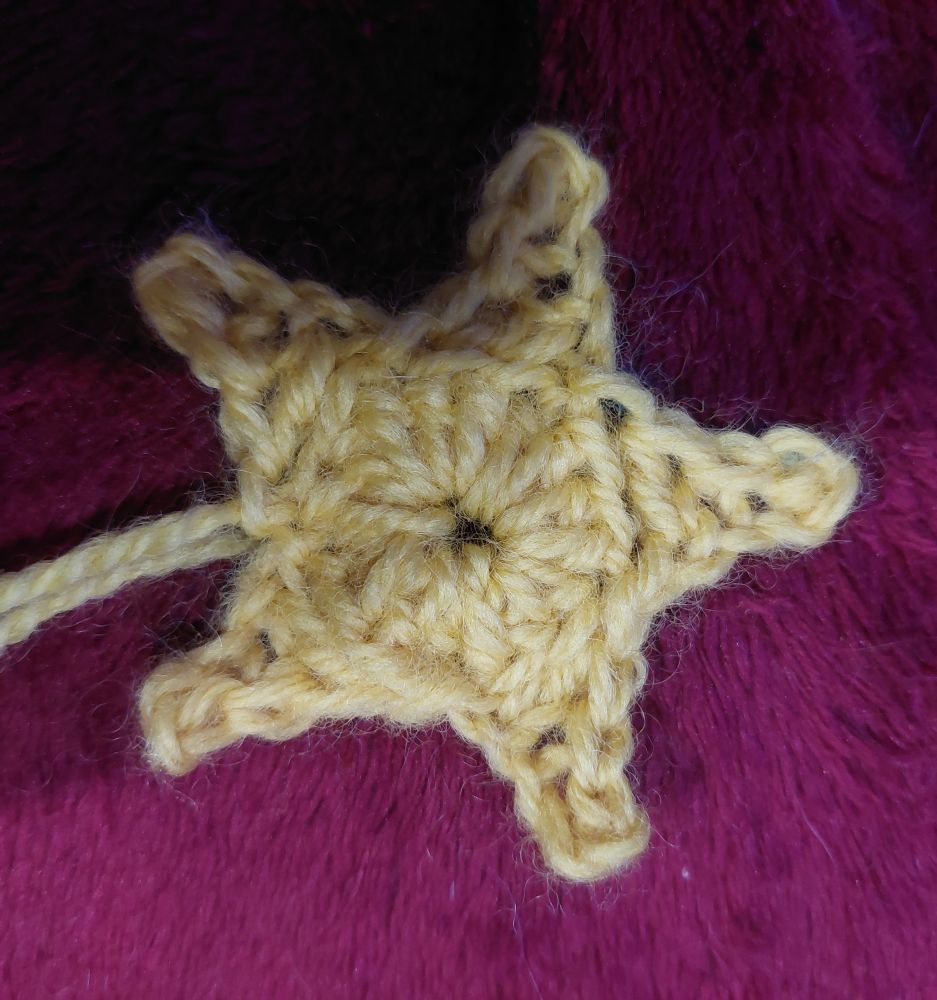 A small star made out of pale yellow yarn on a red blanket background. 