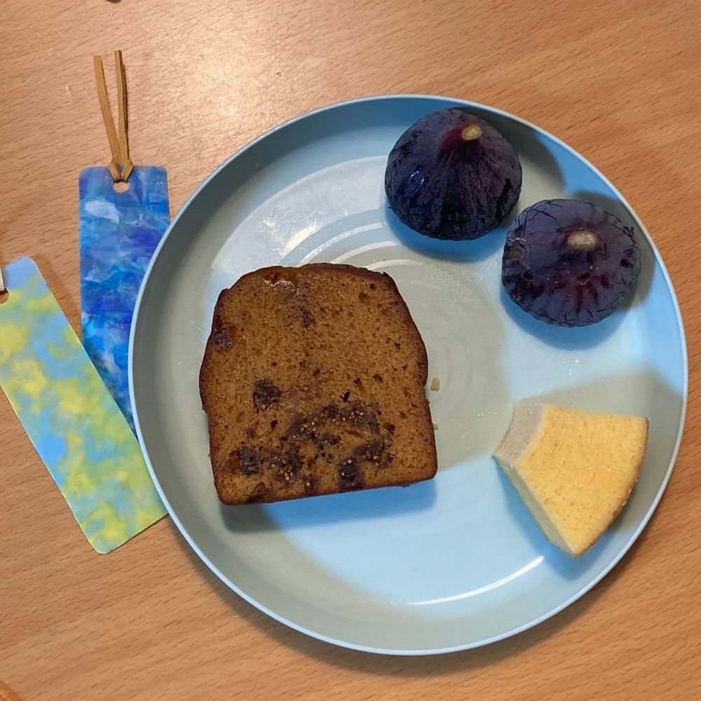 お皿の上にバウムクーヘン一切れ、パウンドケーキ一切れ、黒イチジクふたつ。皿の横にマーブル模様のしおりふたつ。