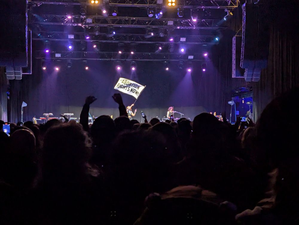 The singer of Sextile on stage performing at The Salt Shed. She is waving a large white flag that says "ABORTION RIGHTS NOW"