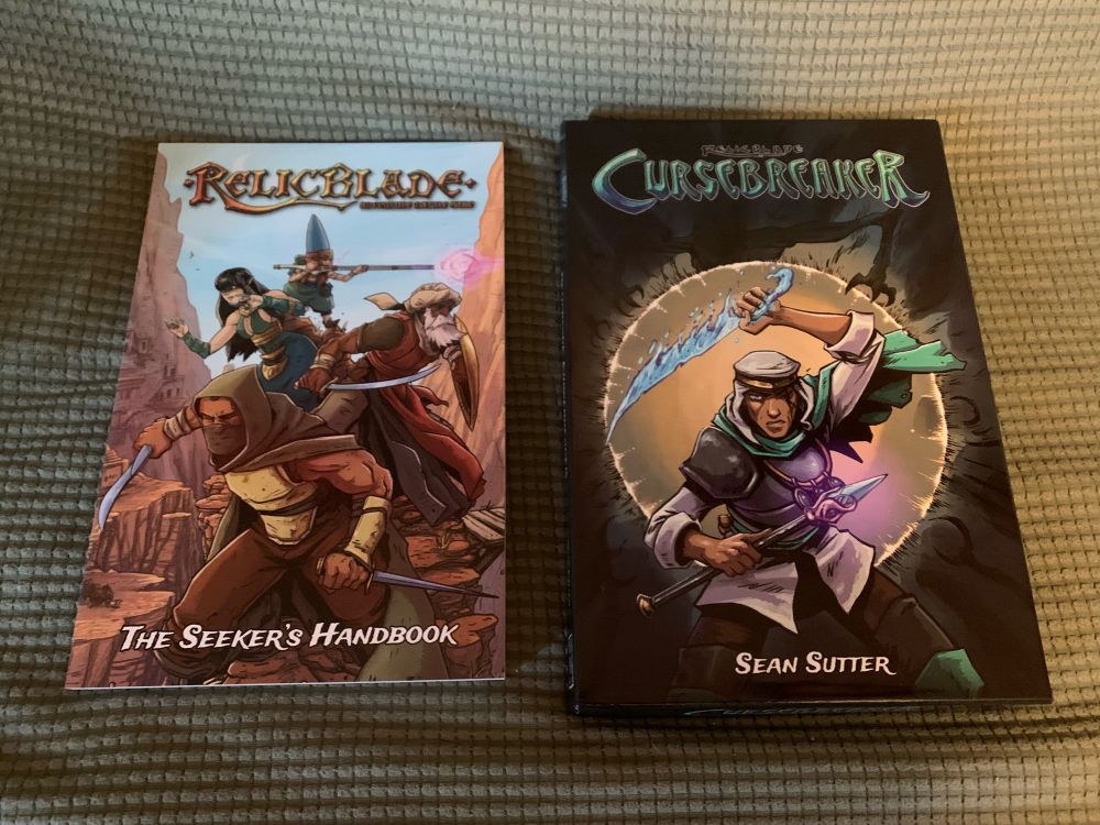 A picture of the Relic Blade core rulebook and the box for Cursebreaker